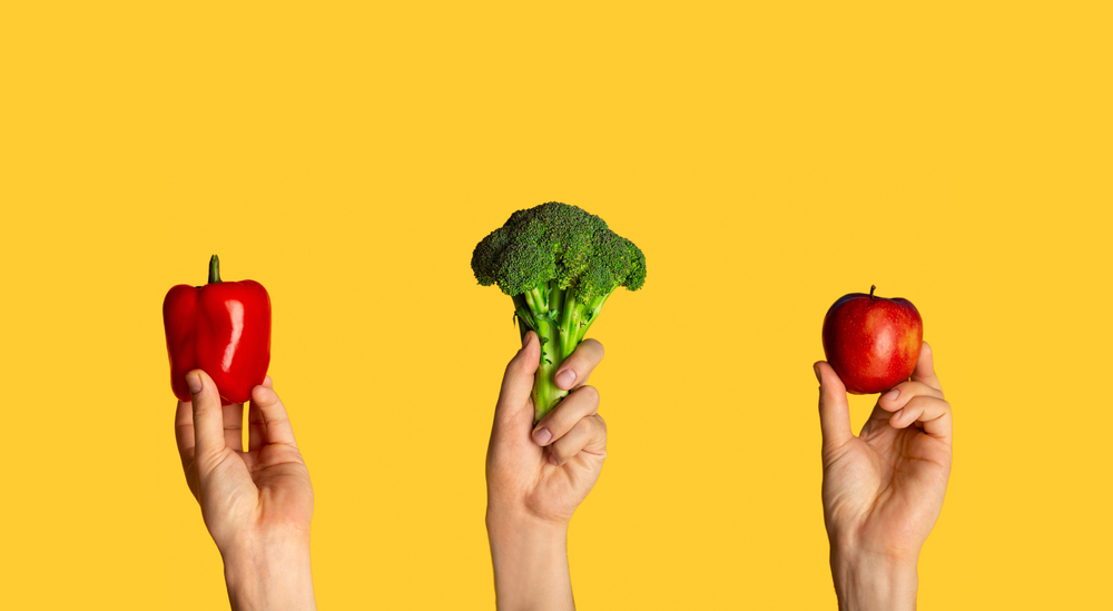 Hands holding broccoli, bell pepper and apple