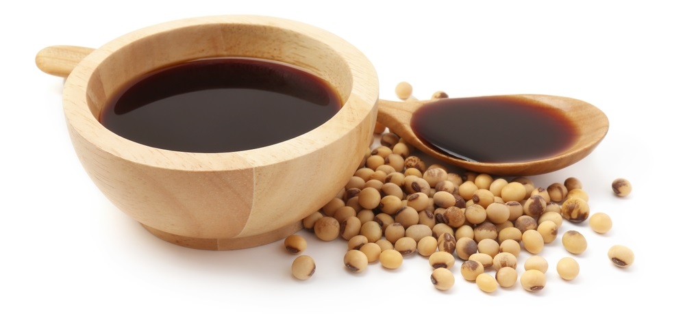 Tasty soy sauce in bowl, soybeans and spoon