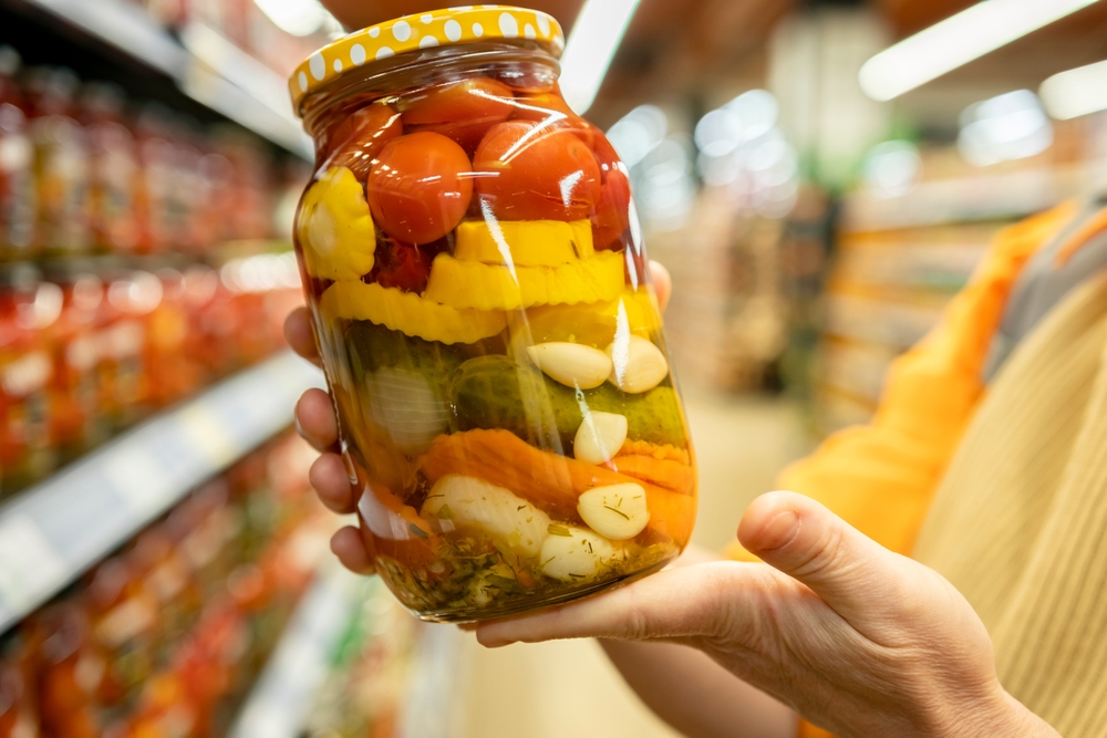 Colorful jar of pickled vegetables packed for flavor stability held by a shopper in a grocery store aisle